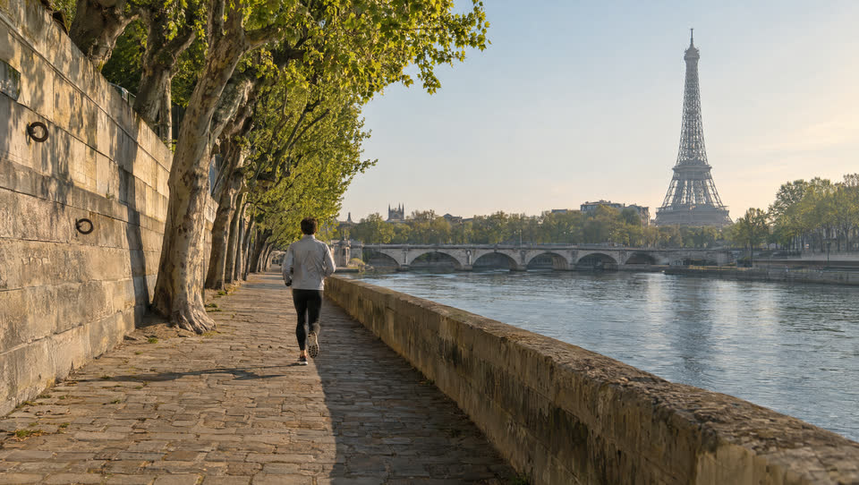 A runner on a stone riverside path in Paris, with the Eiffel Tower ahead