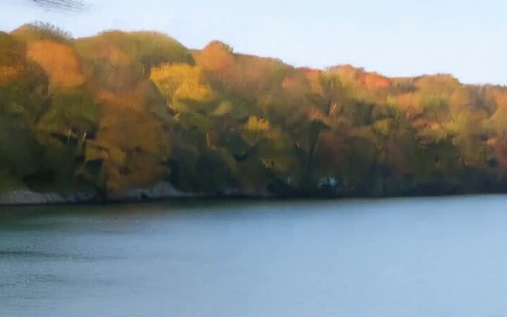 A calm lake below a shore of autumn trees
